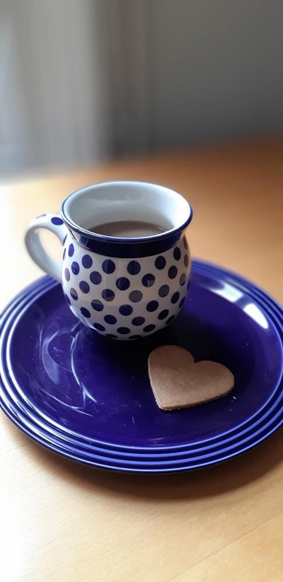 A blue spotted teacup on a blue small plate with a brown heart biscuit.