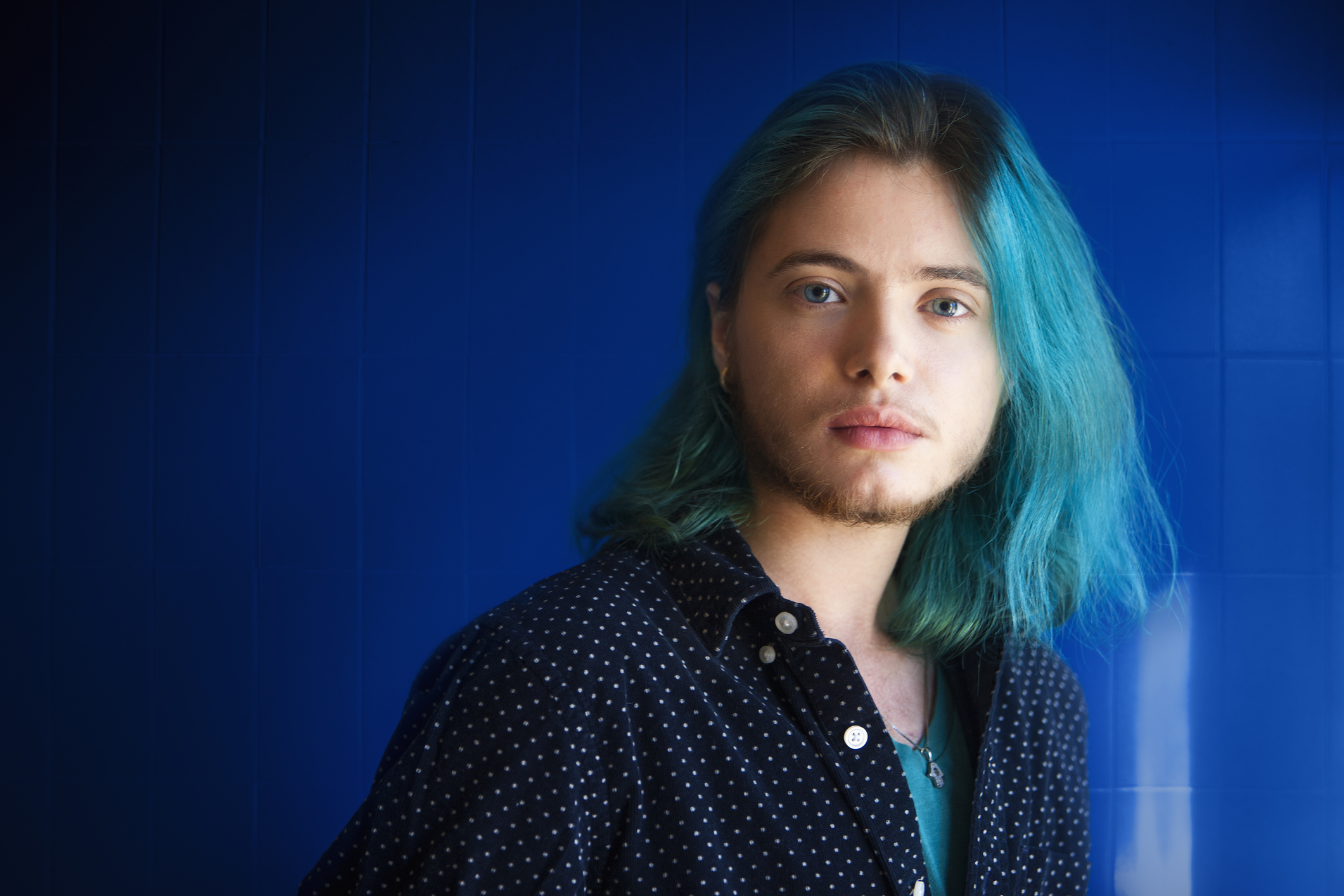 Portrait transgender male in front of blue tiled bathroom wall